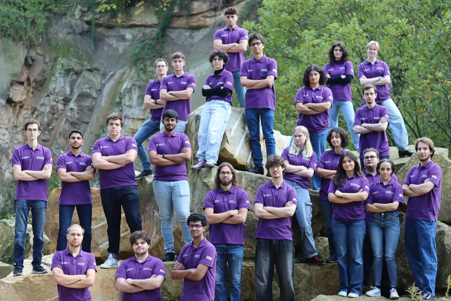 The RoboTeam Twente team in matching purple polos, posing on rocks in a quarry